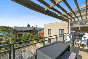 Un balcon doté d’un barbecue et de sièges, offrant une vue sur un quartier résidentiel avec des maisons et des arbres.