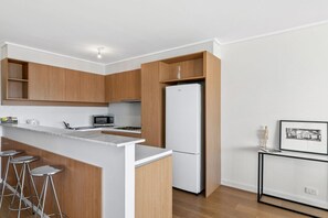Une cuisine moderne avec des meubles en bois, un réfrigérateur blanc, un four à micro-ondes et un coin bar avec des tabourets.
