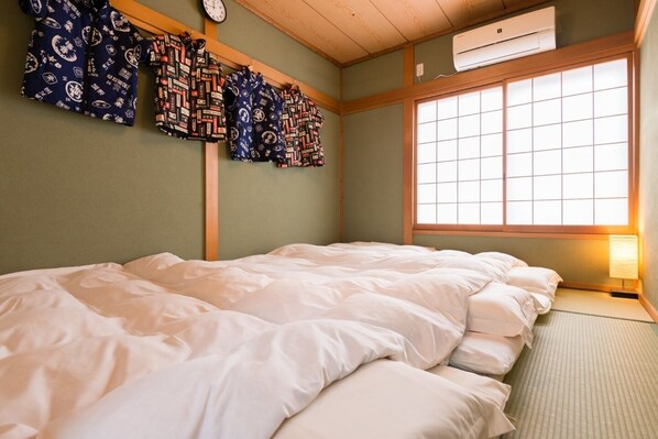 A traditional Japanese-style room with tatami flooring, a futon bed, a shoji screen window, and a wall-mounted clock.