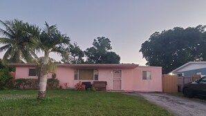 A pink single-story house with a number '332' on the front, a gated driveway, and a palm tree in the front yard. - Jazzy Escapes (with pool) near Hard Rock Stadium (Miami)