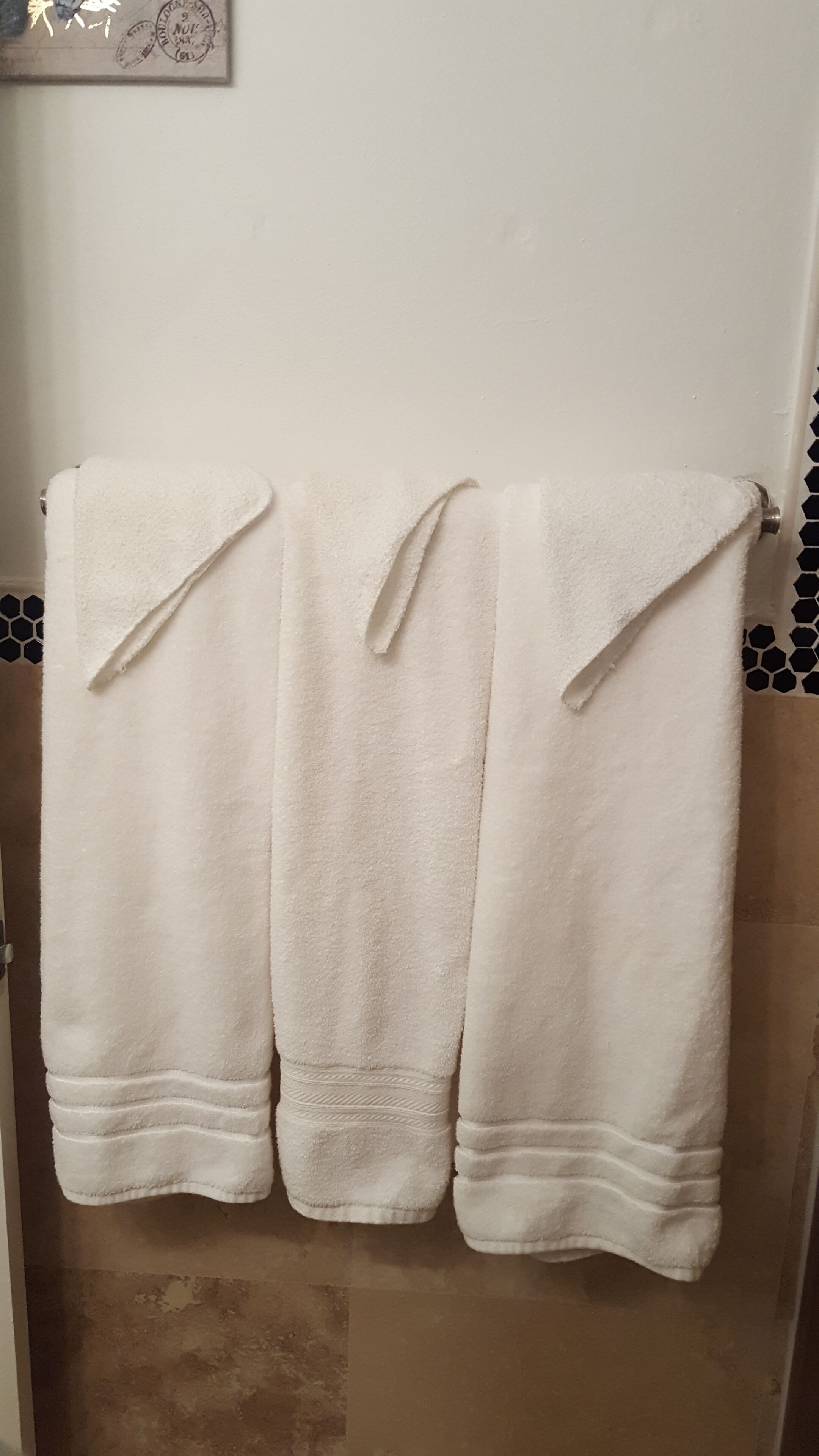 Three white towels hanging on a rack in a bathroom with a hexagonal tile backsplash.