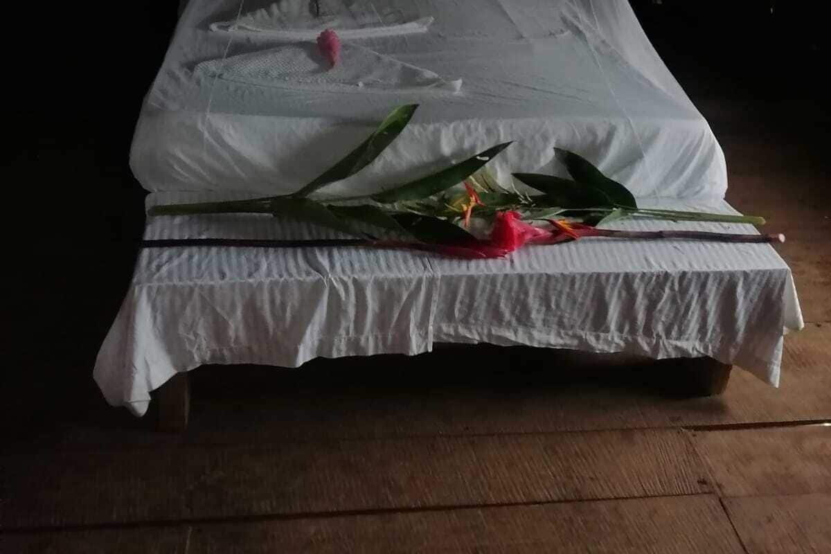 A bed with a canopy, white bedding, and a bouquet of flowers on the side.