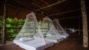 Varias camas con mosquiteras bajo un techo de madera, rodeadas por una terraza de madera y una cerca de madera.