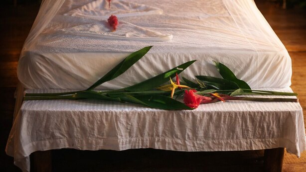 Una cama con dosel, sábanas blancas y un arreglo floral decorativo.
