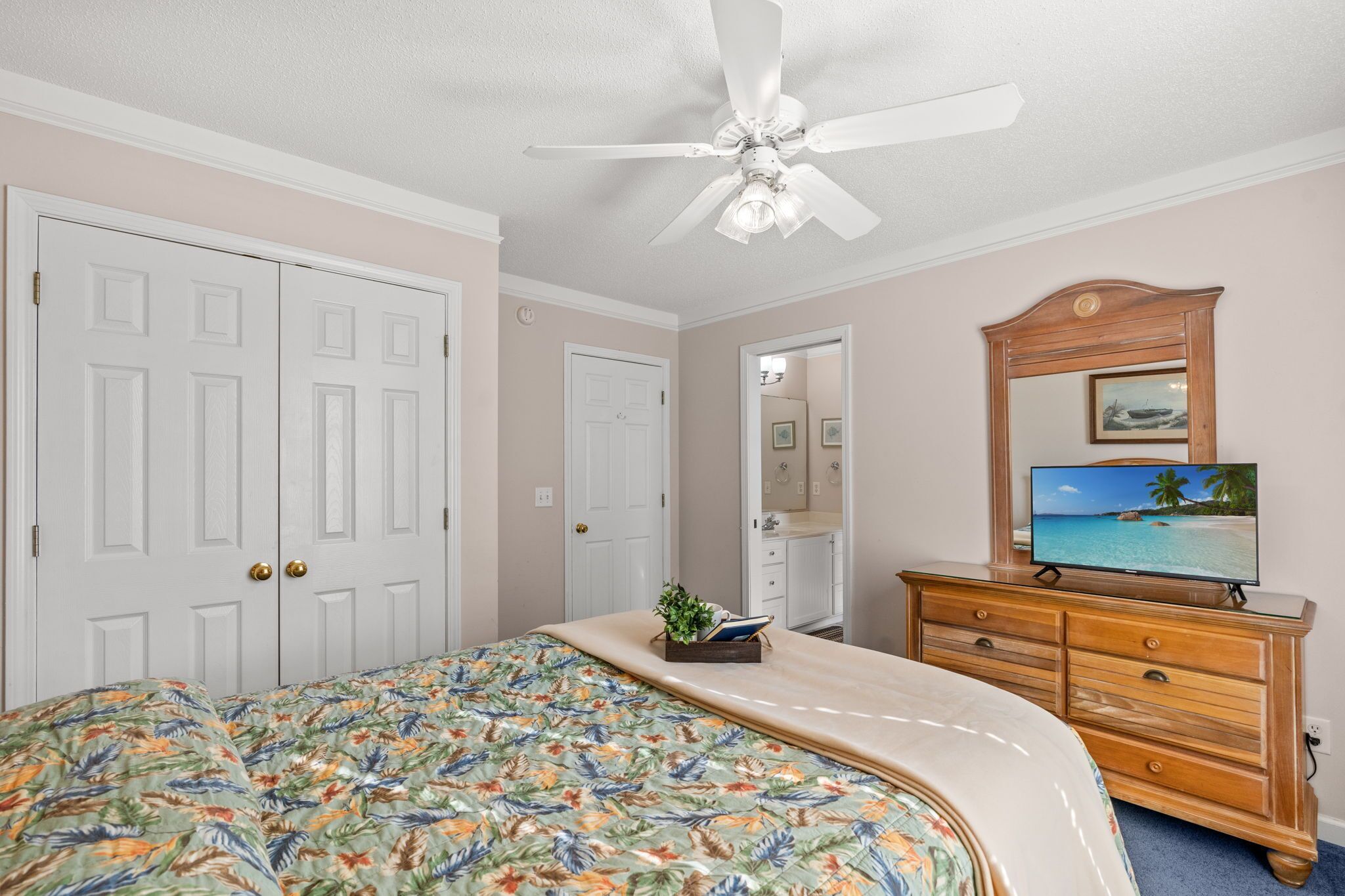 A bedroom with a bed, dresser, ceiling fan, and a television on a dresser.