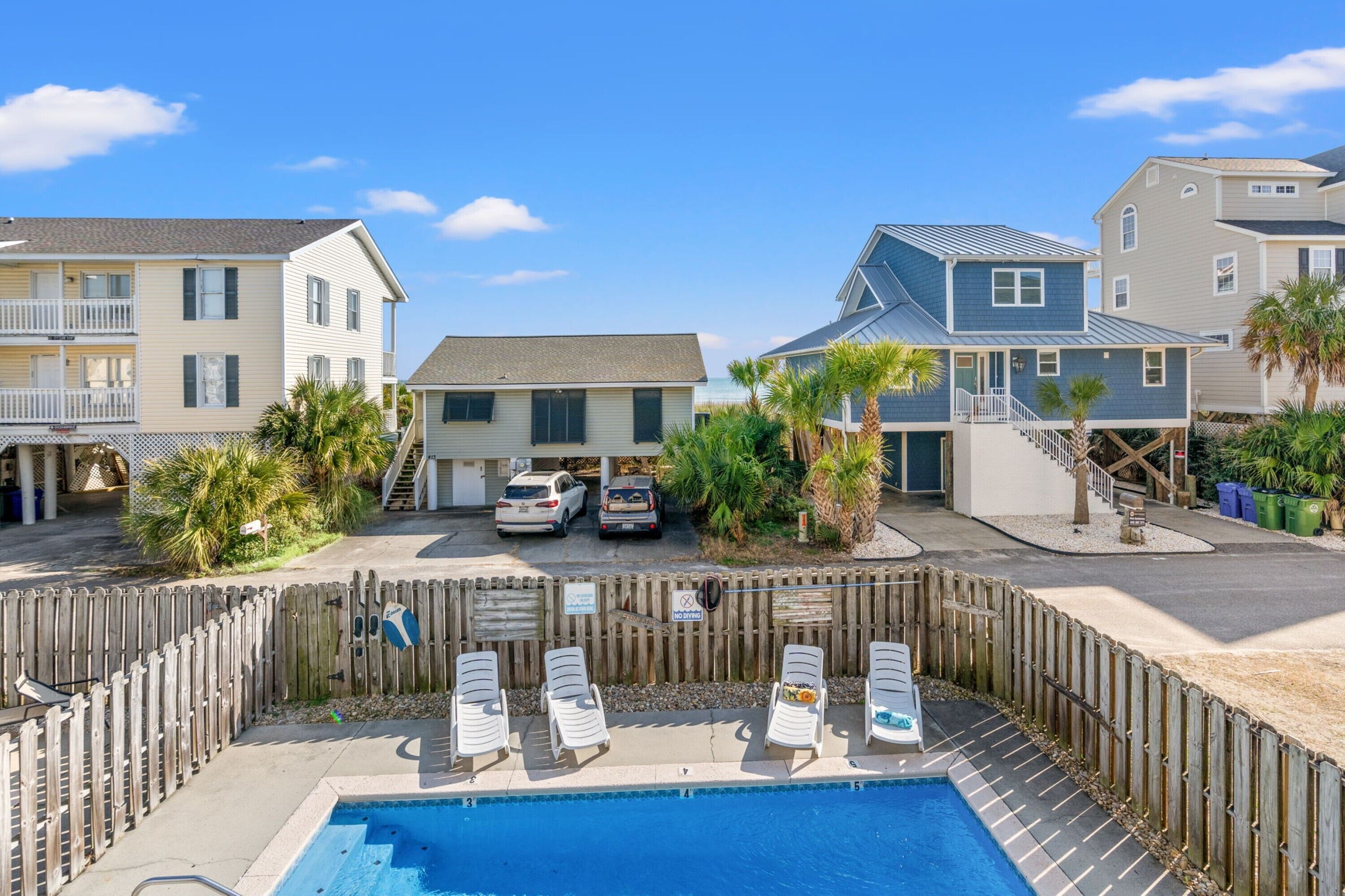 A pool area with lounge chairs, a wooden fence, and a view of adjacent buildings.