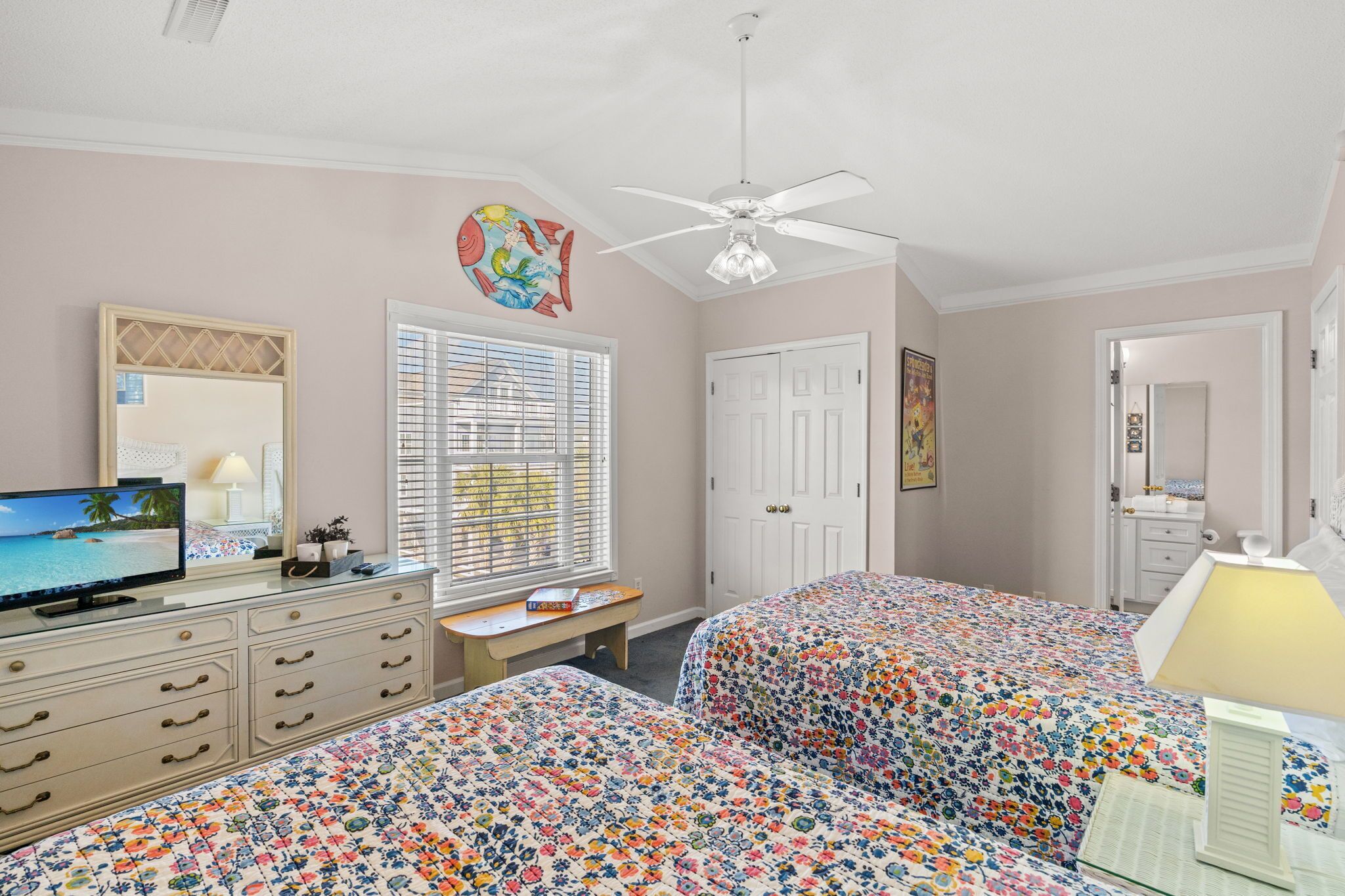 A bedroom with two beds, a TV, a desk, a ceiling fan, and a door.