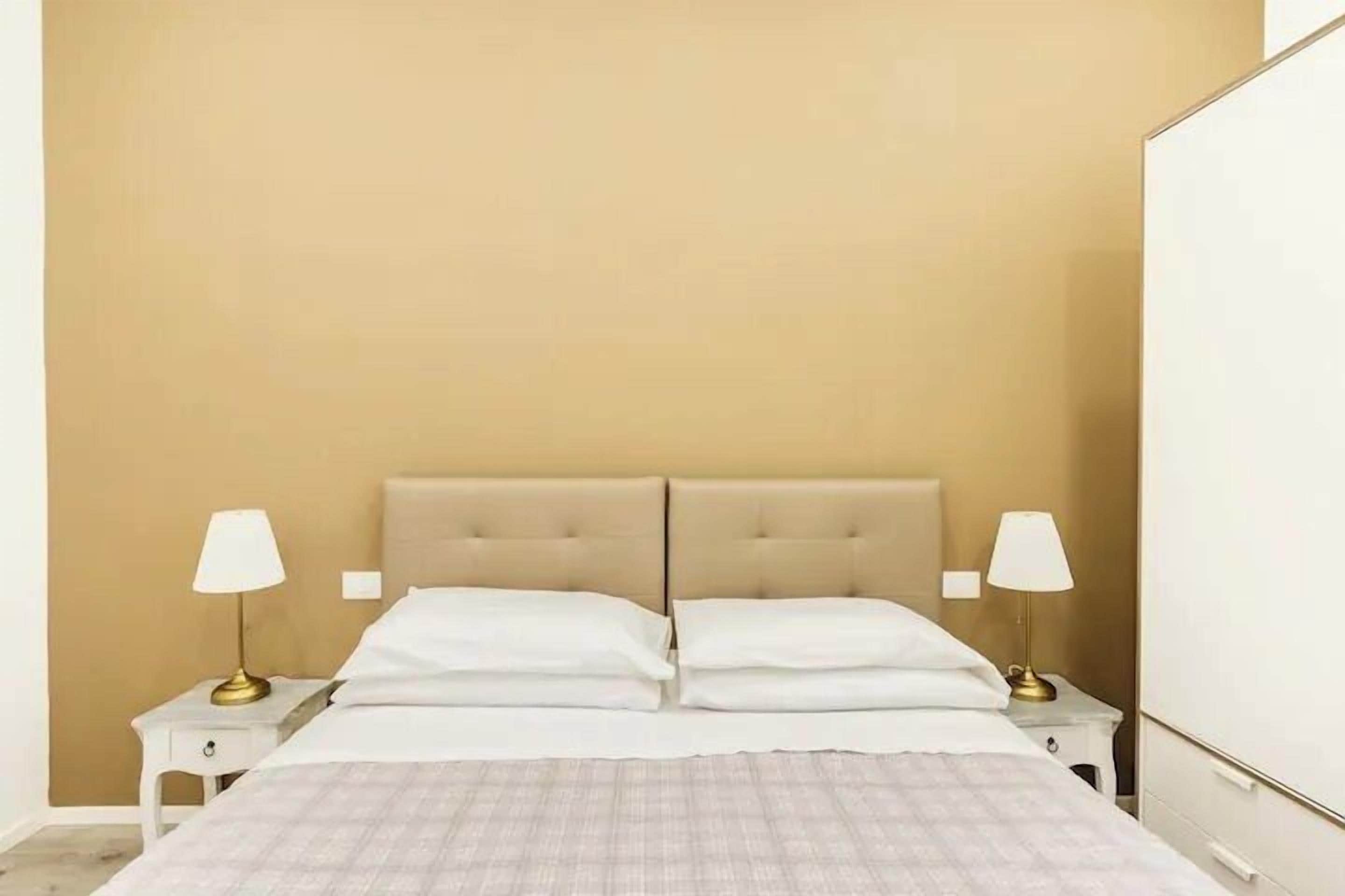 A bedroom with a beige headboard, white bedding, and two bedside lamps.