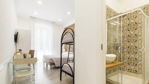 Une salle de bain moderne avec une douche à parois de verre, un lavabo avec un miroir et un lit dans la pièce adjacente.