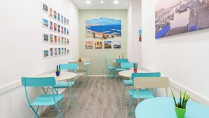 Une pièce avec des chaises et des tables de couleur turquoise, un mur orné de tableaux encadrés et une grande fenêtre donnant sur une ville côtière.