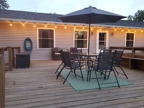 An outdoor deck with a table and chairs, string lights, and an umbrella. - Hilltop Retreat, a modernly-rustic getaway! (Murphysboro)