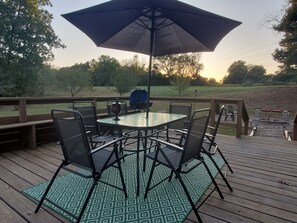 A deck with a glass table and chairs, surrounded by a wooden deck and a green patterned rug. - Hilltop Retreat, a modernly-rustic getaway! (Murphysboro)