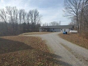 A house with a gravel driveway, a garage, and a large white tank in the yard. - Hilltop Retreat, a modernly-rustic getaway! (Murphysboro)