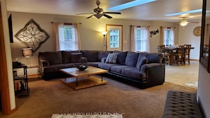 A living room with a sectional sofa, a coffee table, a lamp, and a dining area in the background.