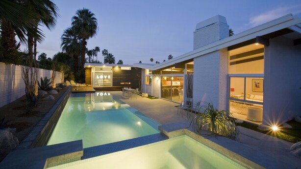 A modern pool area with a clear pool, lounge chairs, and a building with 'LOVE' and 'GOAL' signs. - The Butterfly 4 Bedroom Home, Ideal Downtown Historic Tennis Club location (Palm Springs)
