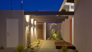 A modern house with a minimalist design, featuring a concrete pathway, a wooden deck, and a small garden with rocks and plants. - The Butterfly 4 Bedroom Home, Ideal Downtown Historic Tennis Club location (Palm Springs)