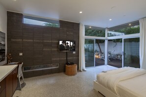 Relax in a spacious bedroom with a large bed, flat-screen TV, and sliding glass door leading to a patio area with outdoor seating.