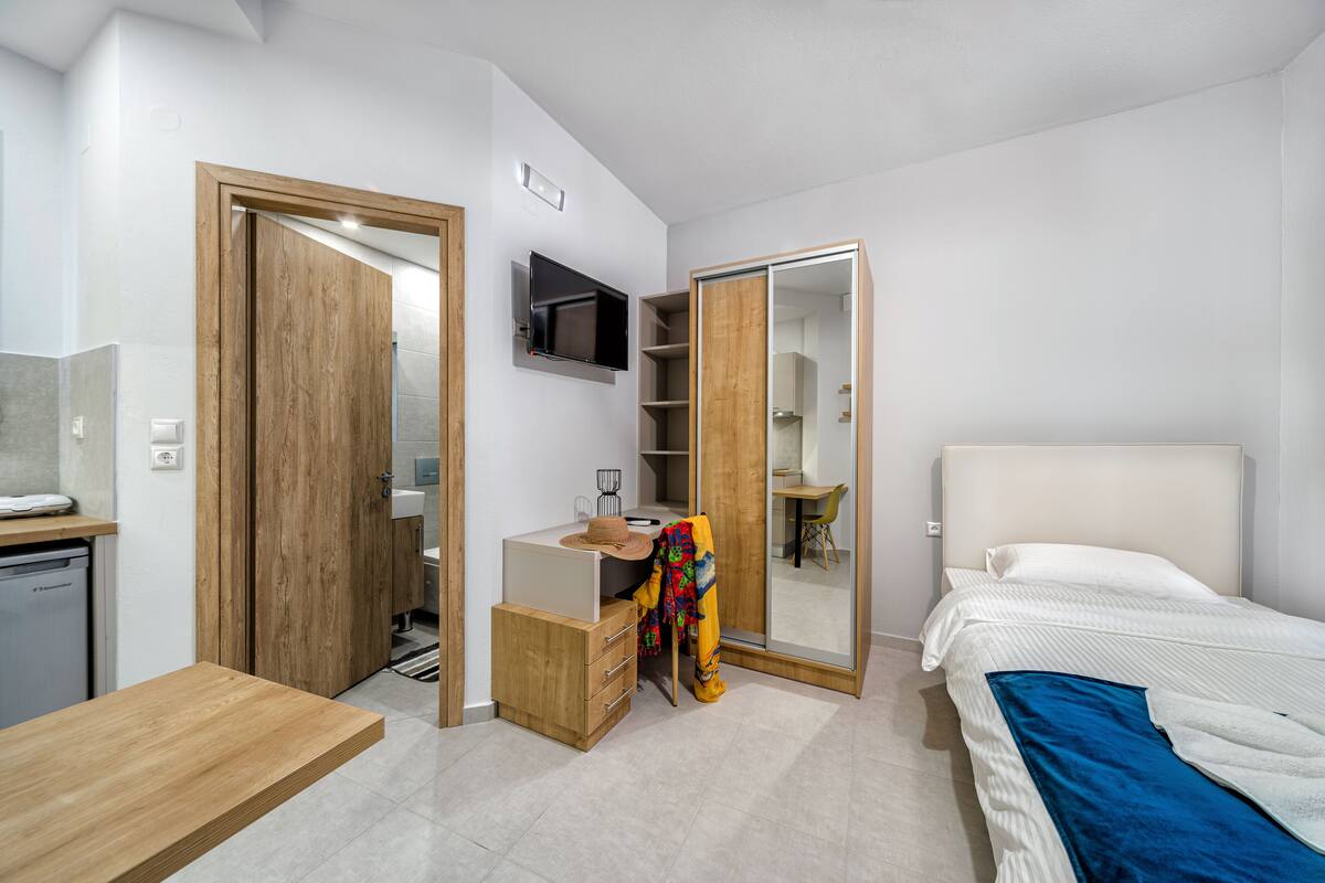 A modern bedroom with a bed, a wooden desk, a mirror, and a wardrobe.