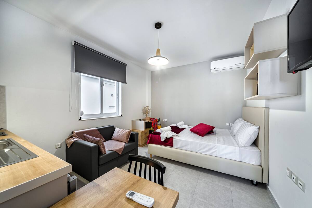 A compact hotel room with a kitchenette, a sofa, a bed, and a dining area.