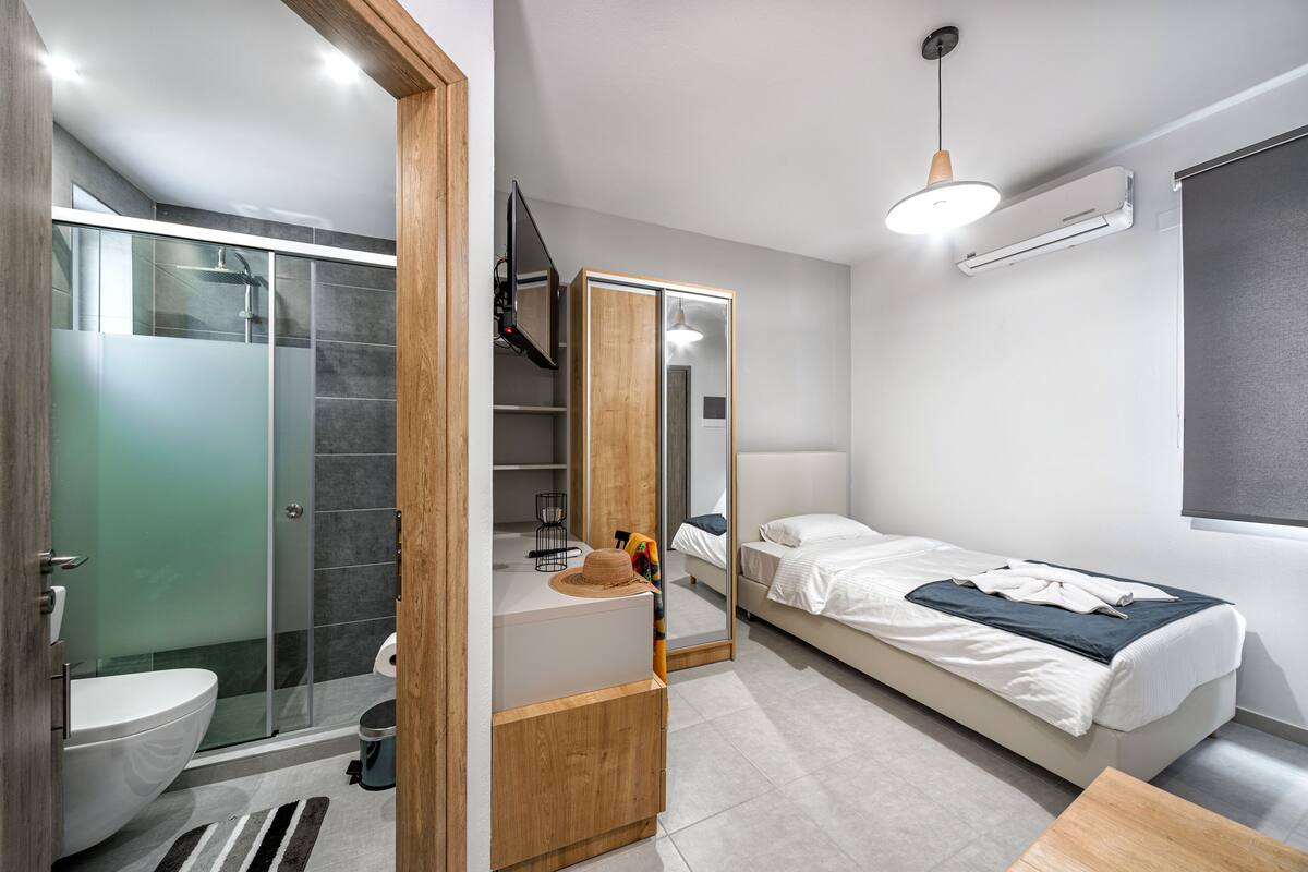 A modern bedroom with a bed, a bedside table, a mirror, and a shower area.