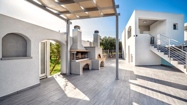 A modern outdoor patio area with a pergola, a barbecue setup, and a staircase leading to an upper level. - Elia Tree Studios (Heraklion)