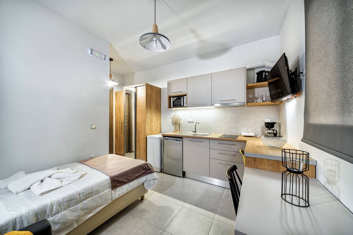 A compact hotel room with a bed, kitchenette, and a TV mounted on the wall.