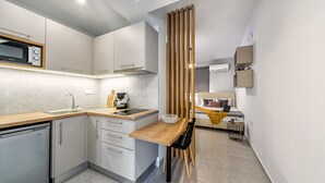 A compact kitchen with a microwave, sink, and modern cabinetry. A dining area with a wooden table and chairs is adjacent to the kitchen. - Elia Tree Studios (Heraklion)