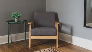 Un fauteuil en bois avec un coussin gris, une petite table ronde avec un pied vert et une plante en pot.