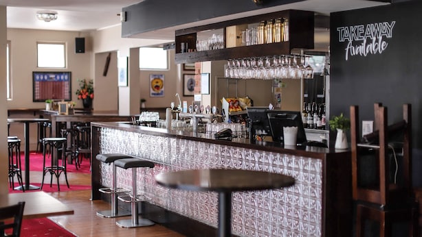 Un espace bar avec des tabourets, un comptoir et un panneau indiquant que les plats sont disponibles à emporter.