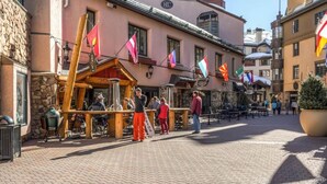 A street with a wooden outdoor seating area, a stone building, and flags. - 413^ One Bedroom - Ski in/out + Ski Valet, 4 Season Pool & Spa! (Beaver Creek)