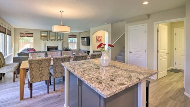 A spacious kitchen with granite countertops, a dining area with patterned chairs, and a central island with a vase of flowers. - Upscale House for 17 with Firepit & Lovely Yard (Star)