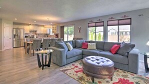 A spacious living room with a grey sectional sofa, a round ottoman, and a dining area with a glass table. - Upscale House for 17 with Firepit & Lovely Yard (Star)