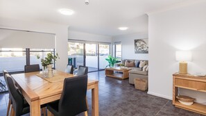 Relax in this inviting living area with a dining table for four, comfortable sofa, and large windows offering a view of the outside.