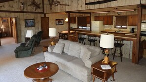 A rustic interior with a sofa, chairs, a coffee table, and a kitchen area with bar stools. -  Cassel, Ca. on Hat Creek. Close/Baum Lake, Burney, Mt. Shasta/Lassen 3 nite min (Cassel)