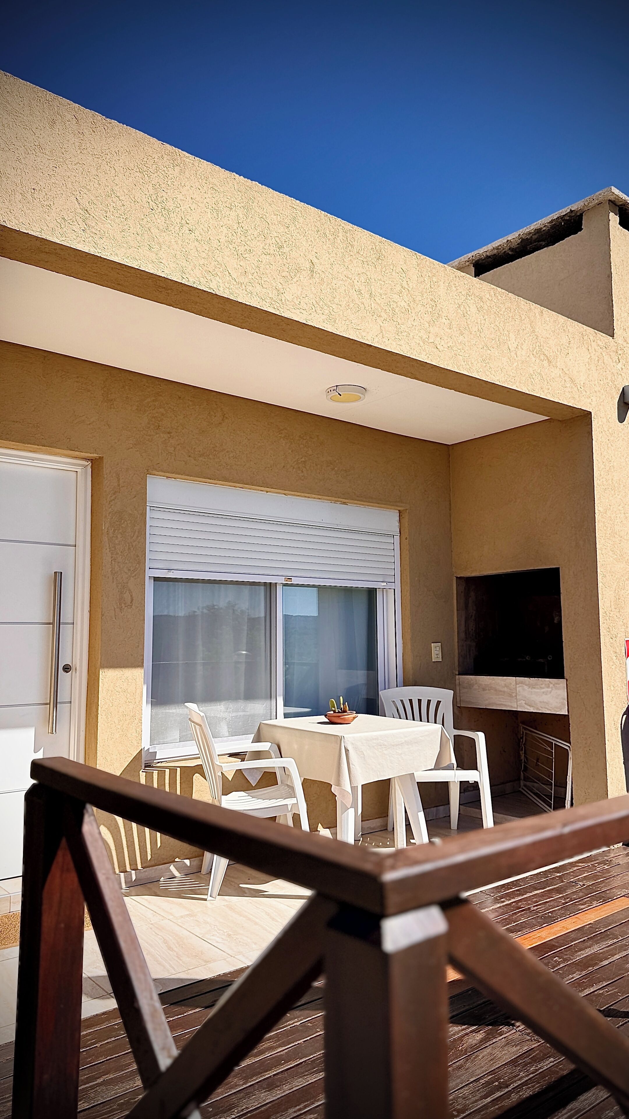 Un patio con mesa y sillas, una ventana con persianas y un televisor montado en la pared.