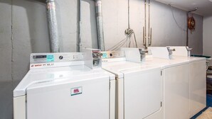 A laundry area with stacked washers and dryers, metal pipes on the wall, and a blue floor mat.