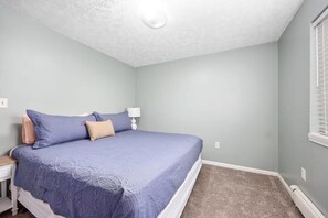 Un dormitorio con cama, mesita de noche y ventana con persianas.