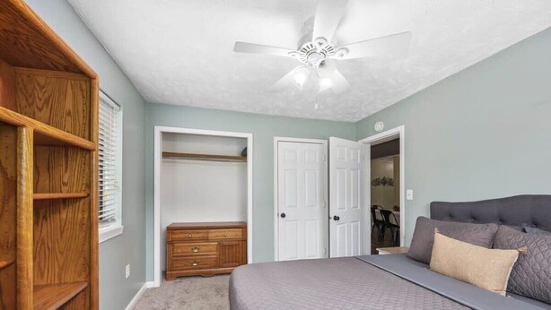 A bedroom with a bed, a ceiling fan, a wardrobe, and a door leading to another room.
