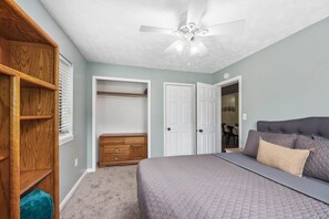 Une chambre à coucher comprenant un lit, un ventilateur de plafond, une armoire en bois et une porte donnant sur une autre pièce.