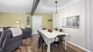 A compact living space with a dining area, a sofa, and a kitchen visible through an open door.