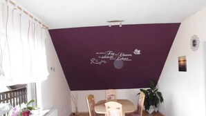 A dining area with a table and chairs, a window with curtains, and a decorative wall with a quote. - Apartment Angela (Bad Sachsa)
