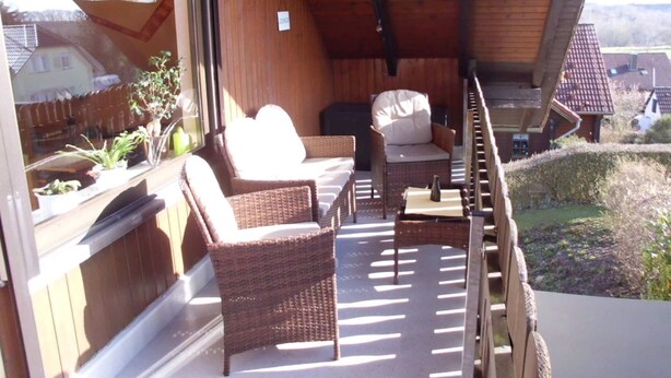 A covered outdoor seating area with wicker furniture and a view of the surrounding landscape. - Apartment Angela (Bad Sachsa)