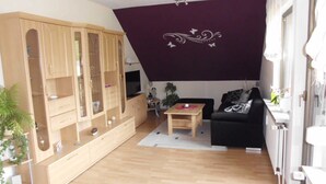 A living room with a wooden cabinet, a black sofa, a small table, and a TV. - Apartment Angela (Bad Sachsa)