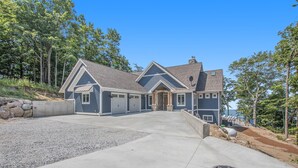 A modern two-story house with a front entrance, a driveway, and a landscaped area with trees and a stone wall.