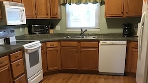 A kitchen with wooden cabinets, a microwave, stove, dishwasher, and a window with curtains.