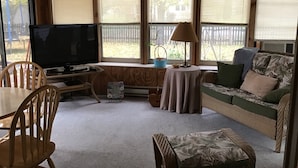 A cozy living room with a television, a sofa, a table, and a window with blinds.