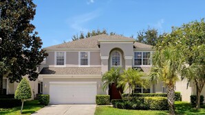 A two-story house with a garage, a well-maintained lawn, and palm trees. - Disney Home, Huge Patio 6B/4B -Pool& SPA-FREE HEAT (Kissimmee)