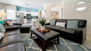 A modern living room with a sectional sofa, a coffee table, and a dining area with a kitchen in the background. - Disney Home, Huge Patio 6B/4B -Pool& SPA-FREE HEAT (Kissimmee)