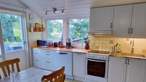 A modern kitchen with white cabinetry, a wooden dining table, and a view of greenery outside. - Lovely cottage with large terrace by the sea and nature. (Bräkne-Hoby)