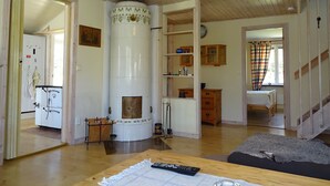 A living room with a fireplace, wooden furniture, and a kitchen area visible through an open door. - Lovely cottage with large terrace by the sea and nature. (Bräkne-Hoby)
